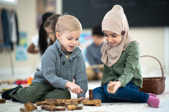 A multi-ethnic group of kindergarten friends smile as they play with blocks in their classroom.